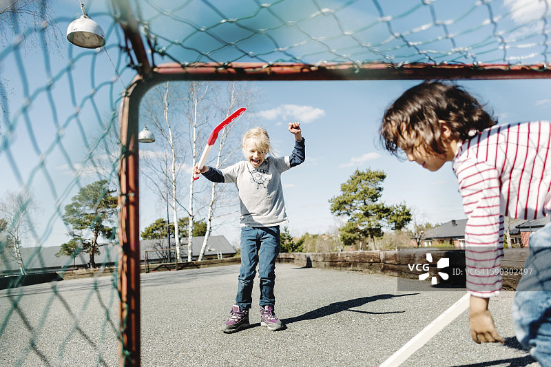 开心的女孩在院子里和男孩一起玩曲棍球时做手势图片素材