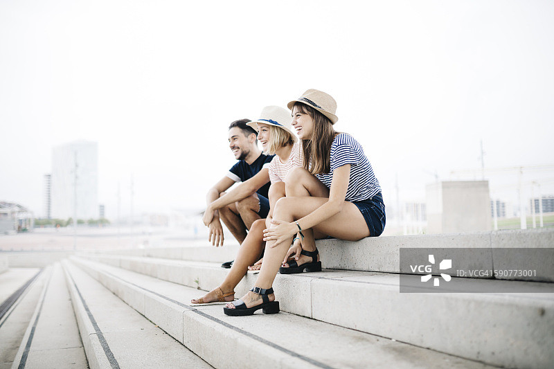 西班牙巴塞罗那坐在楼梯上并排坐着的三位欢笑的朋友图片素材