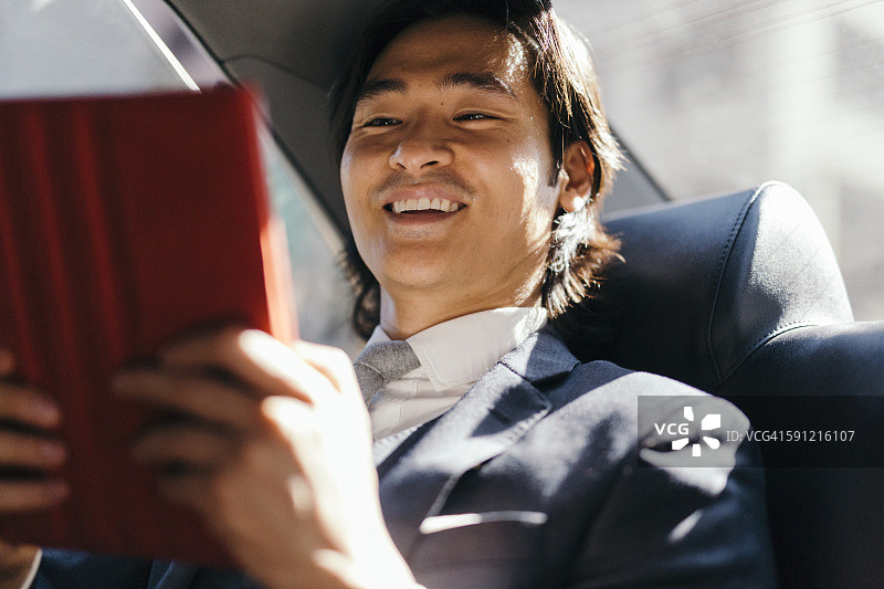 在汽车后座使用平板电脑的面带微笑的商人图片素材