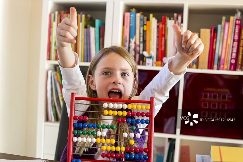坐在算盘后竖起大拇指的欢呼雀跃的女孩肖像图片素材