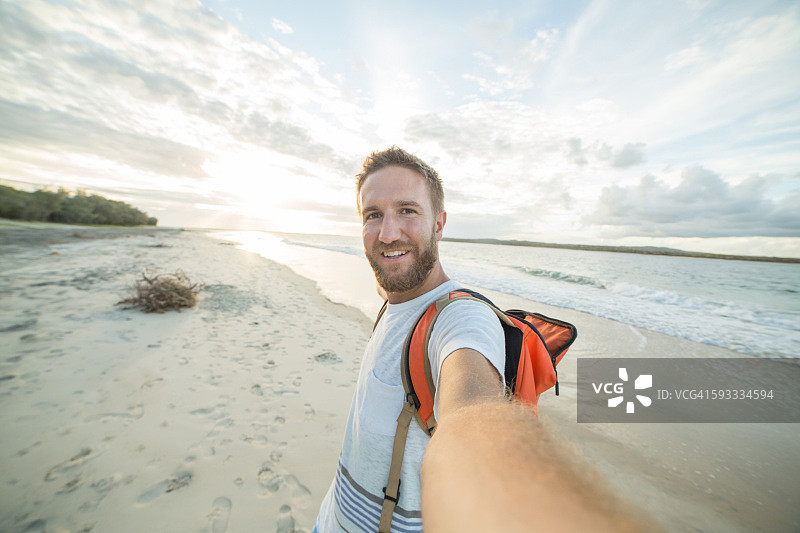 快乐的年轻男人在海滩日落时自拍图片素材