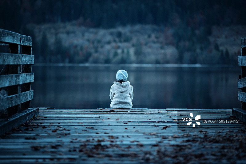 年轻女孩独自坐在黑暗前的甲板旁图片素材
