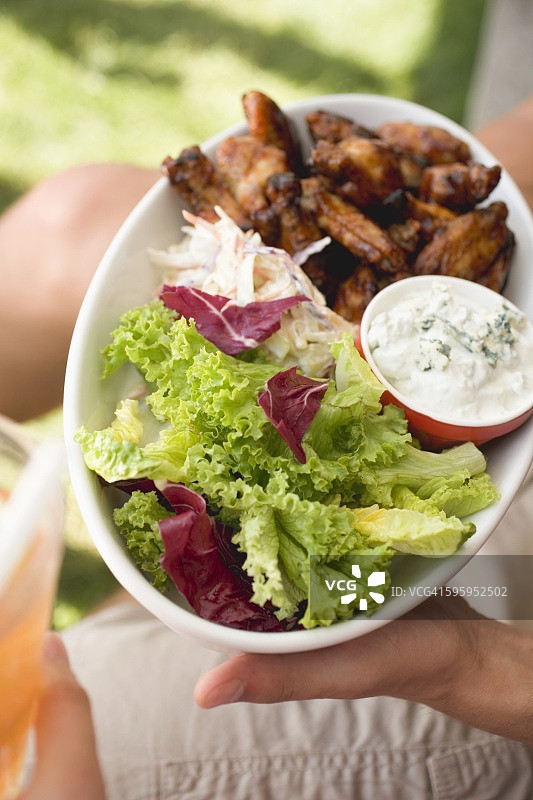 手拿蘸蓝纹奶酪酱和沙拉的炸鸡翅图片素材