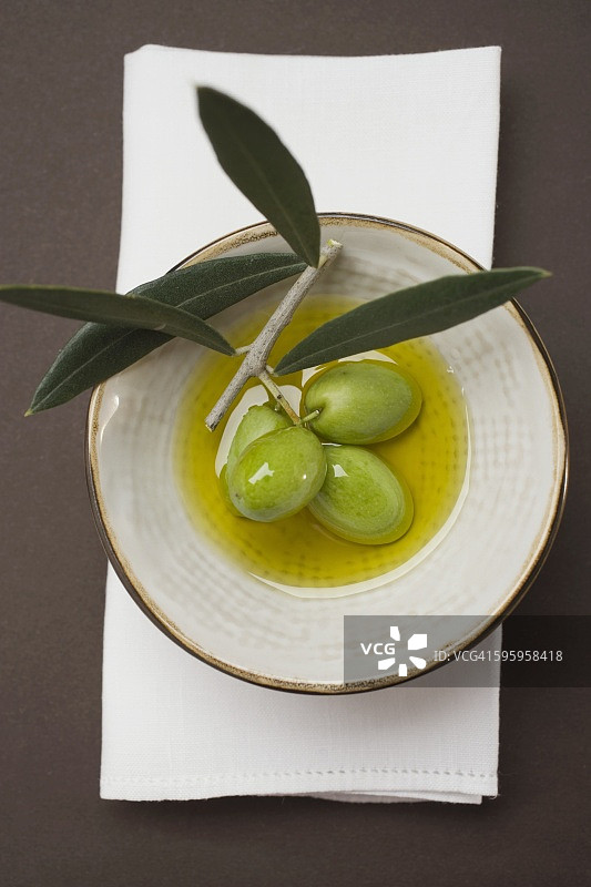 橄榄油碗里带枝的绿色橄榄（俯视）图片素材