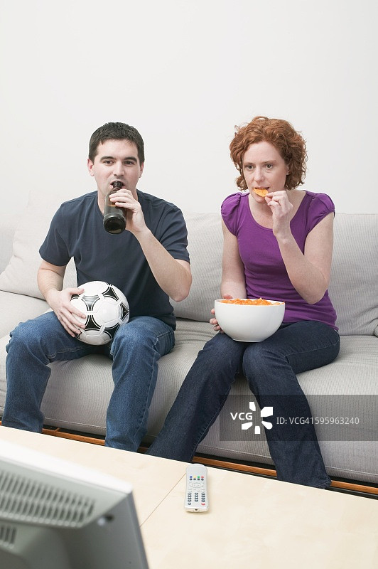 年轻夫妇在看电视，配有足球、啤酒和薯片图片素材