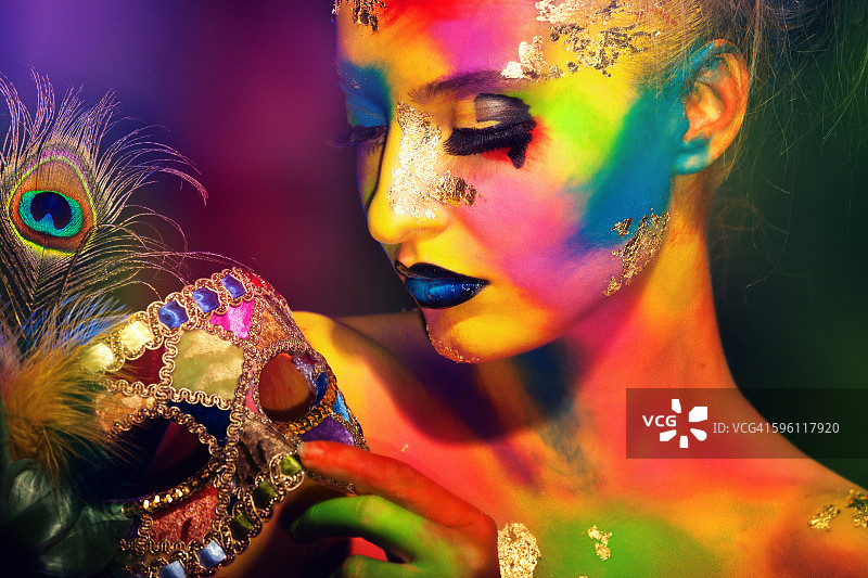 身绘彩色人体彩绘，手持孔雀羽毛装饰的威尼斯面具的女人图片素材