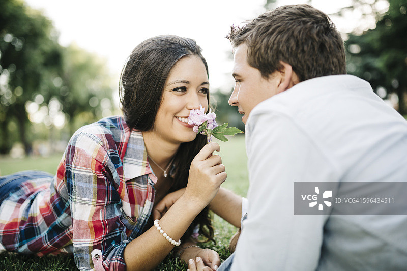 在公园的草地上，年轻情侣脸对着脸躺着。图片素材