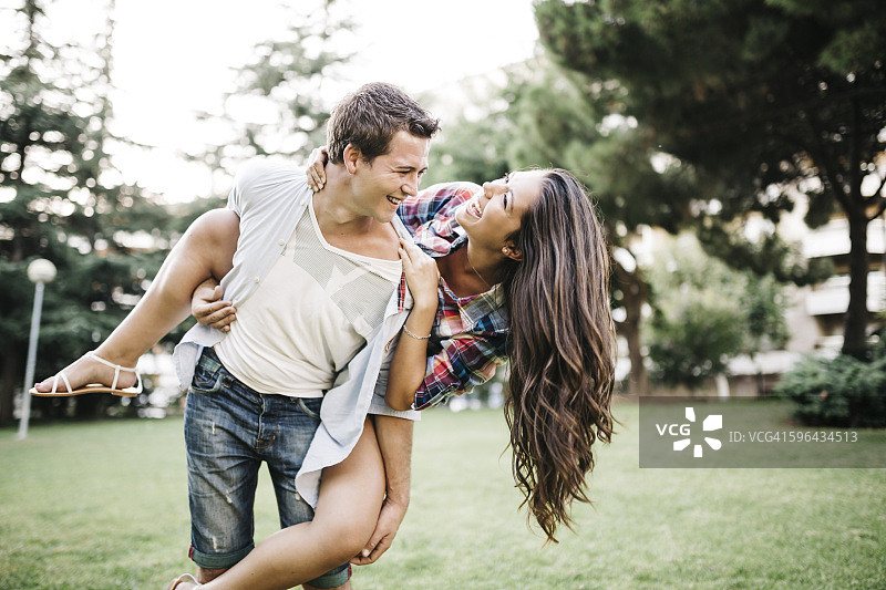 年轻男人在公园草地上背着他的女友图片素材