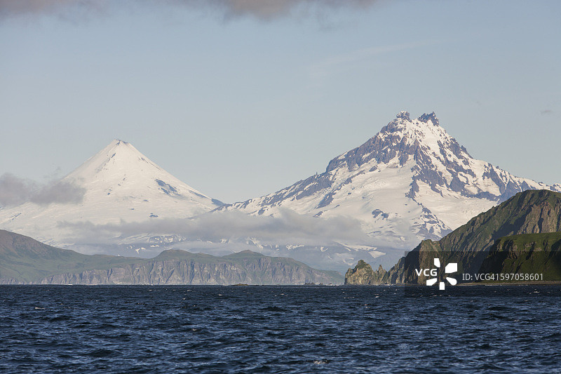 乌尼马克岛潘科夫角崎岖悬崖海岸背景下的希沙尔丁火山和伊萨诺茨基峰，东阿留申群岛图片素材