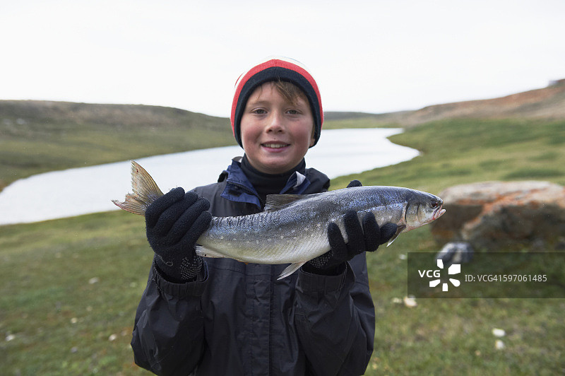 男孩在剑桥湾附近拿着新鲜捕获的北极红点鲑图片素材
