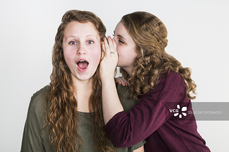一个朋友在白色背景上向另一个朋友说悄悄话的影棚照片图片素材