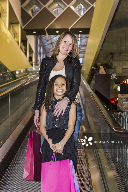 年轻的母亲和她的女儿在购物中心使用自动扶梯。图片素材