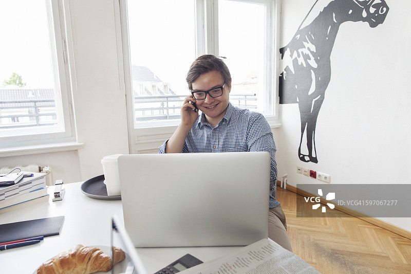 在现代办公室使用笔记本电脑和手机的微笑商务男士图片素材