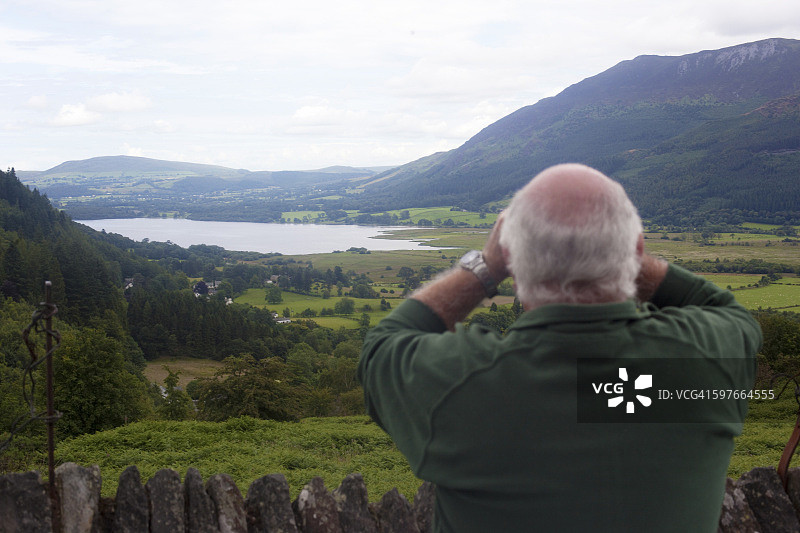 男子在英国坎布里亚郡布雷斯韦特村和惠尼拉特之间的观景点观鸟的背影图片素材