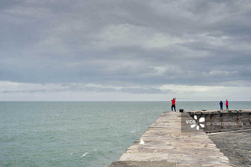 渔民在英国坎布里亚郡的港口墙上抛竿图片素材