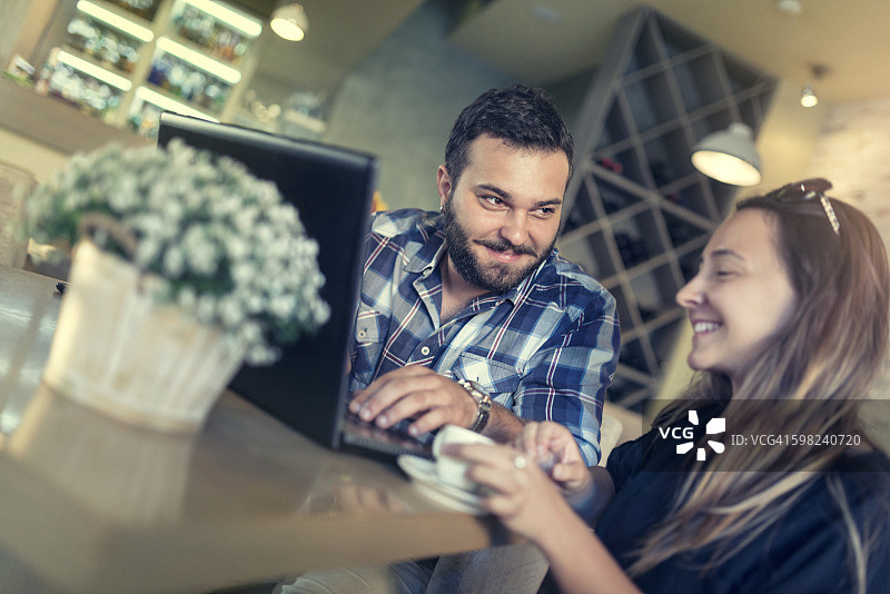 在餐厅喝咖啡时使用笔记本电脑的年轻情侣图片素材