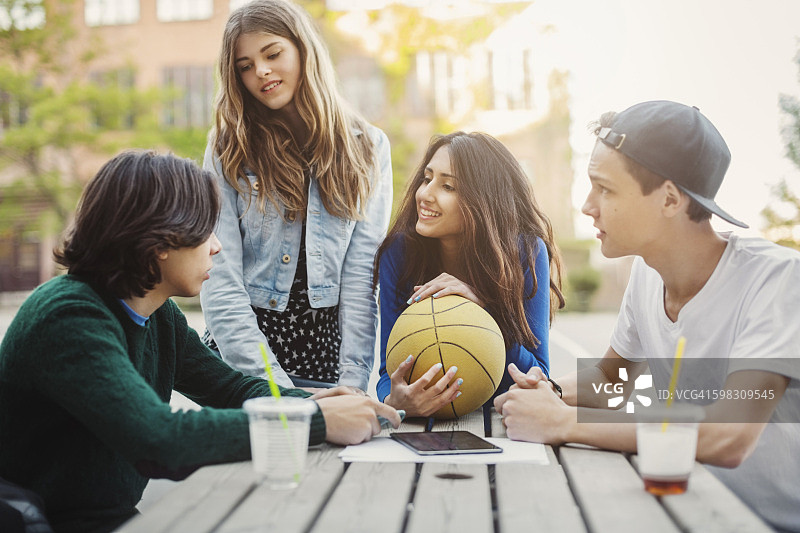 在户外餐桌旁讨论的快乐青少年图片素材