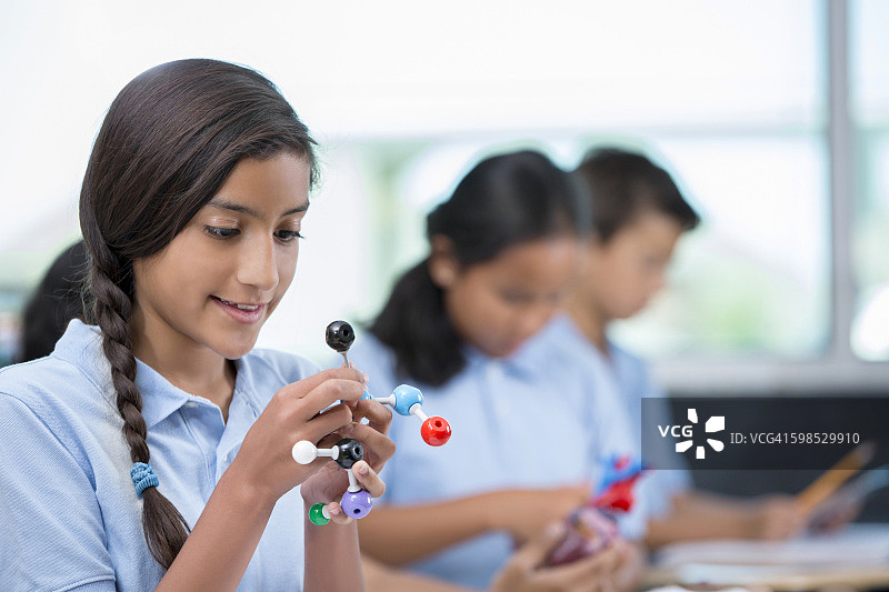 年轻的西班牙裔女学生在科学课上看着分子模型图片素材