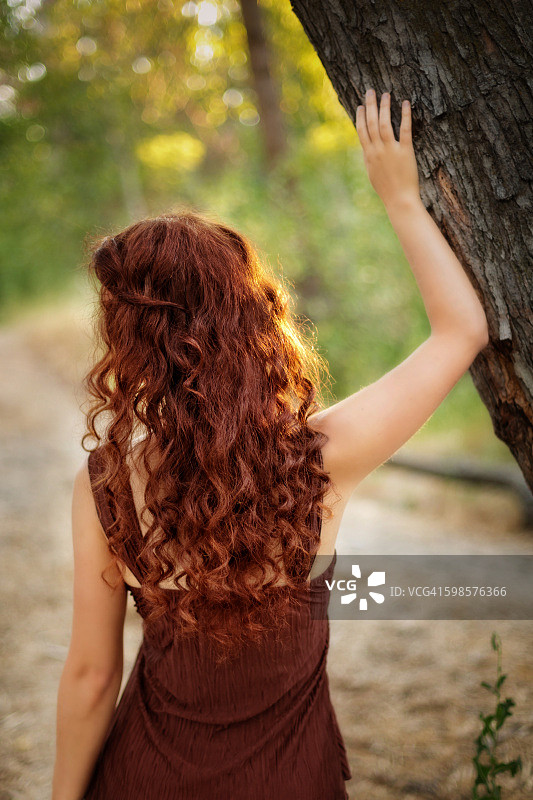 森林中触摸树干的红发女子背影图片素材