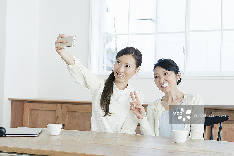 母女在桌旁用手机拍摄自画像图片素材
