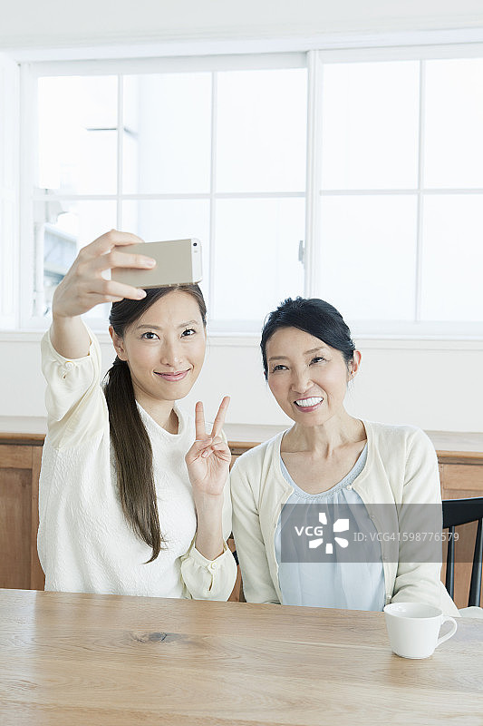 母女在桌旁用手机拍摄自画像图片素材