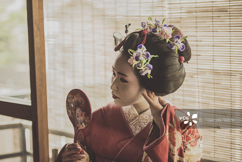 用手镜整理发型的年轻艺伎图片素材