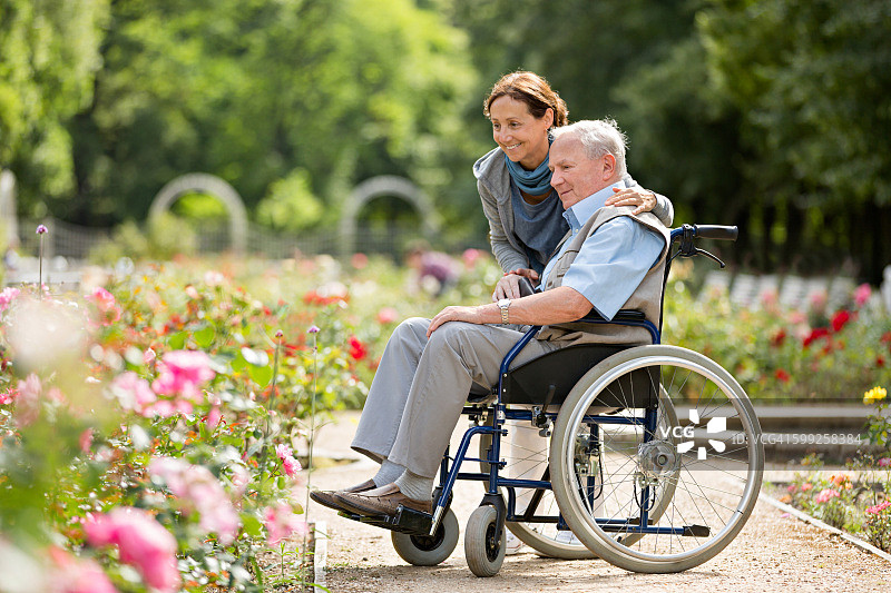 护理人员和坐轮椅的老年男子在公园散步图片素材