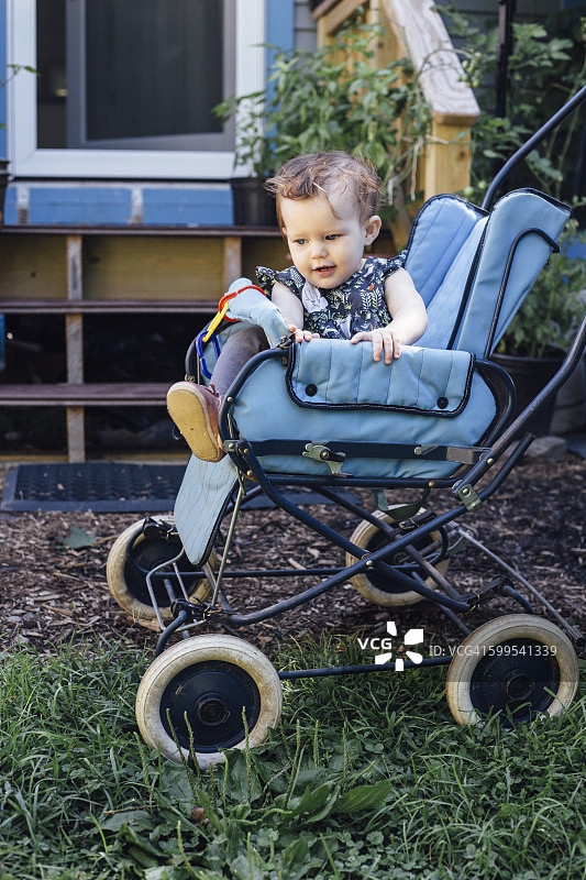 蓝色复古婴儿车里的可爱女婴在门廊外图片素材