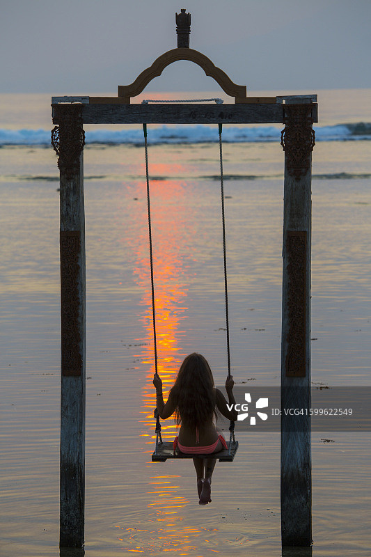 在印度尼西亚龙目岛吉利特拉旺安岛海上秋千上看日落的女性游客图片素材