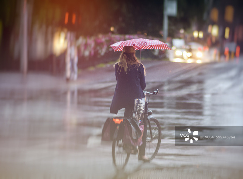 在阿姆斯特丹，一位女士在雨中骑自行车，撑着一把红色雨伞图片素材