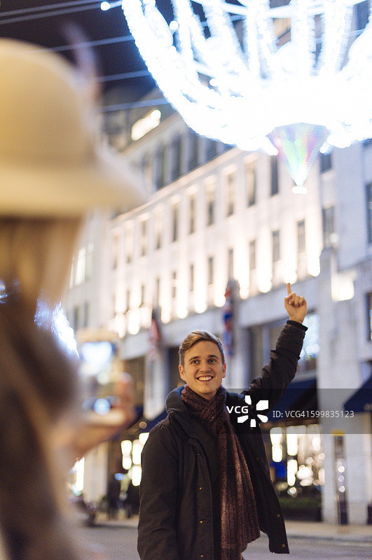 年轻情侣在英国伦敦新邦德街指向圣诞灯饰图片素材