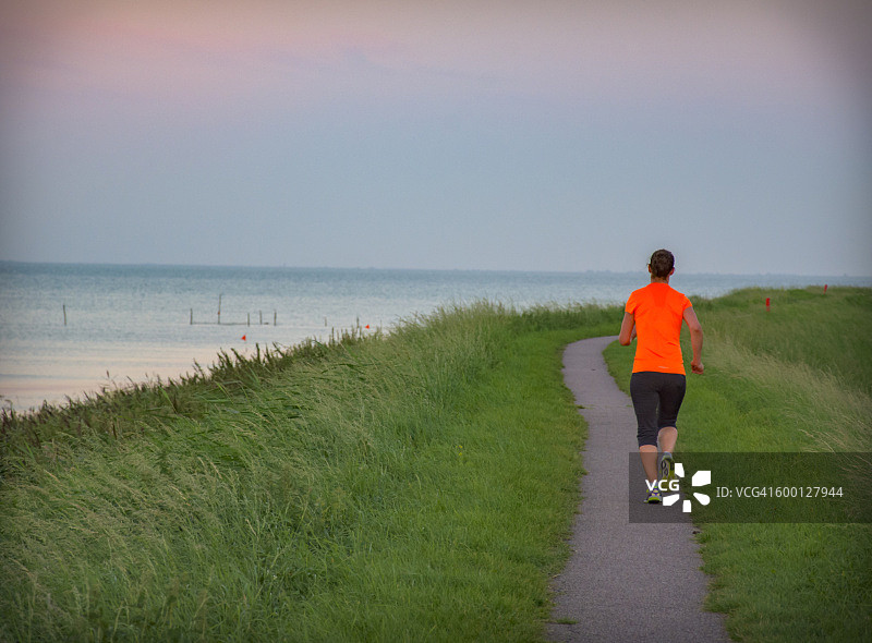乡村小路上跑步的女人背影，左侧是海图片素材