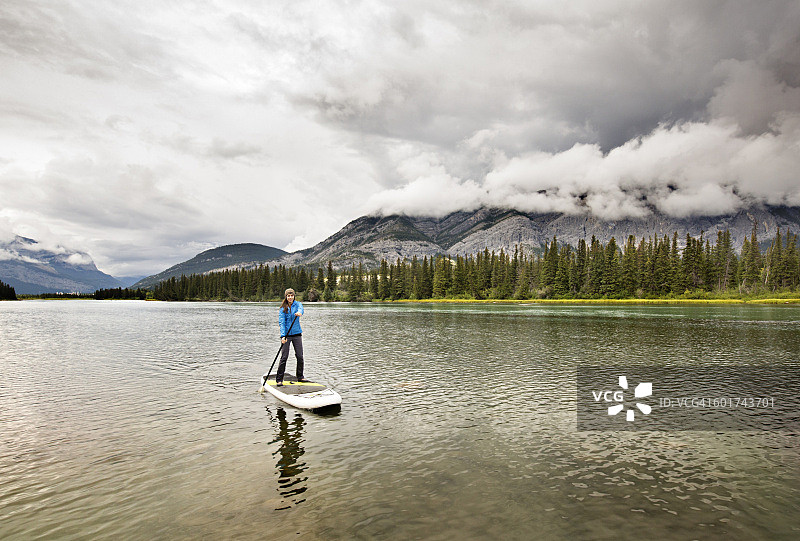 穿着蓝色夹克的女人站在河上的桨板上图片素材