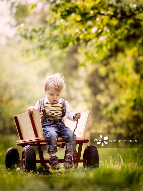 男孩坐在花园里的玩具车上图片素材