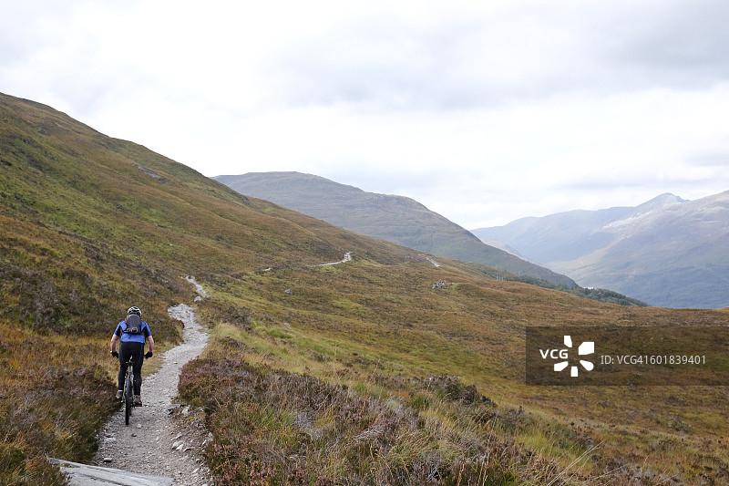 男子在苏格兰高地骑山地自行车的背影图片素材