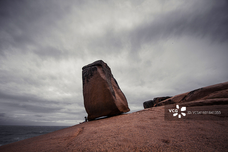 男孩坐在巴西圣卡塔琳娜州拉古纳海滩的Pedra do frade岩石旁图片素材