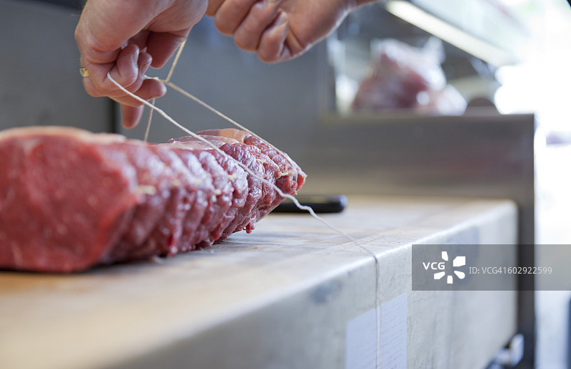 肉铺师傅在砧板上捆扎肉块特写图片素材