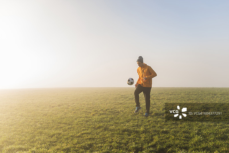 年轻男人傍晚在草地上踢足球图片素材
