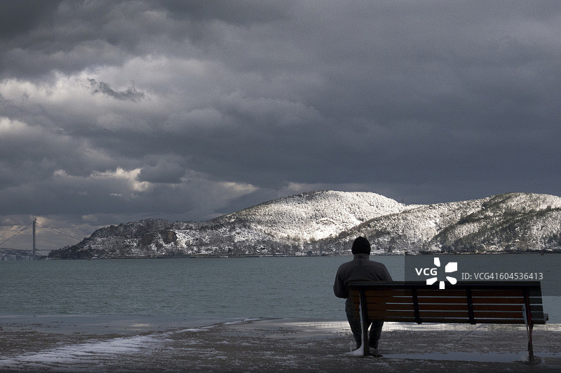 孤独的男人坐在伊斯坦布尔博斯普鲁斯海峡的长椅上图片素材