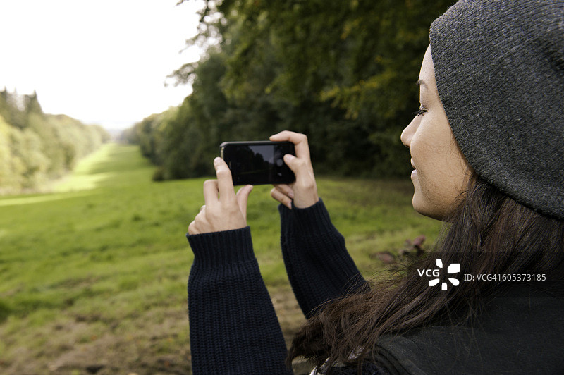 年轻女子用智能手机拍摄田野图片素材