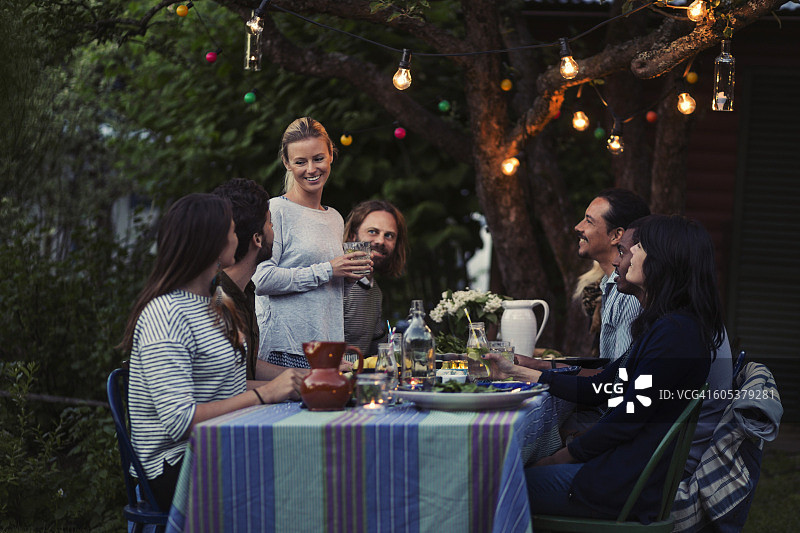快乐的女人在院子里与朋友们在餐桌旁聊天图片素材