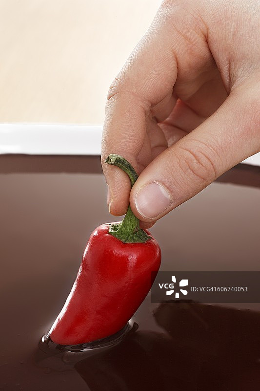 手蘸巧克力酱的红色辣椒图片素材