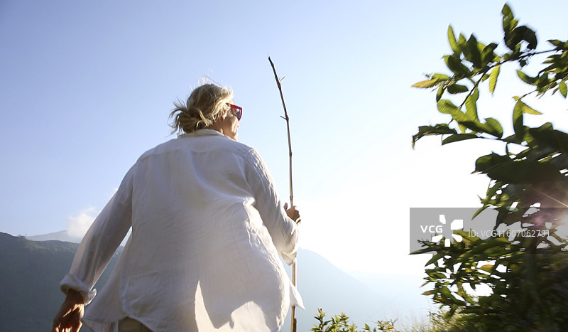 沿着山路徒步，手持竹竿的女人图片素材