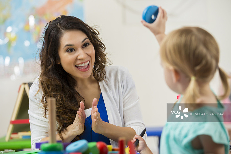 漂亮的西班牙裔教师为可爱的金发学龄前儿童鼓掌图片素材