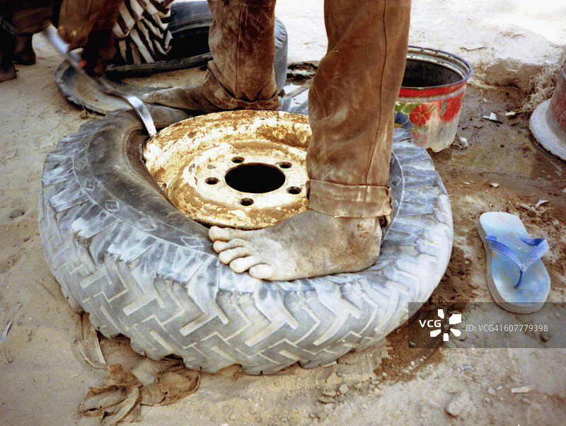 非洲北非撒哈拉沙漠乍得湖地区：赤脚男子试图修理轮胎图片素材