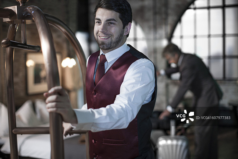 行李员推着手推车，商务男士在背景中，酒店房间图片素材