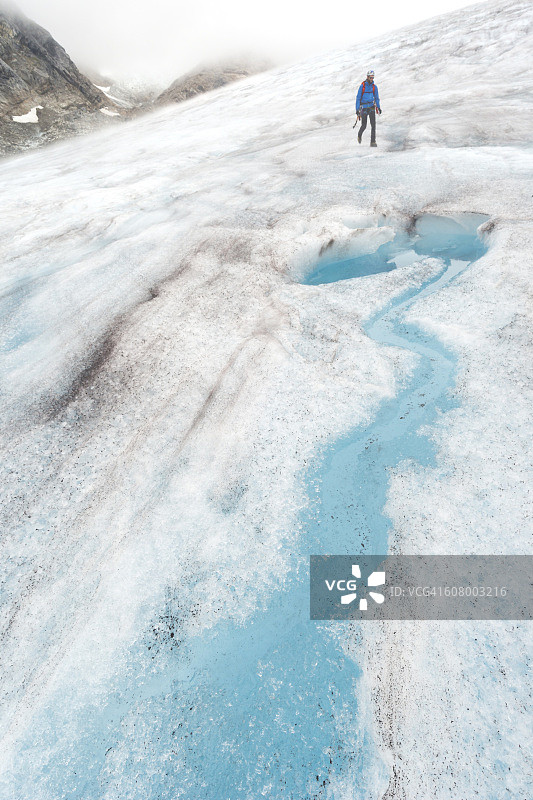 男人在冰川上的倾斜冰面上徒步图片素材