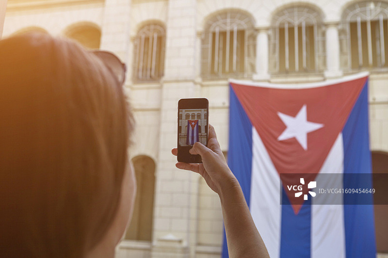 年轻女性在古巴哈瓦那用手机拍摄古巴国旗（肩上视角）图片素材