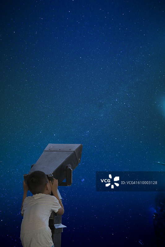 小男孩在敞开的窗户边用望远镜看夜空图片素材