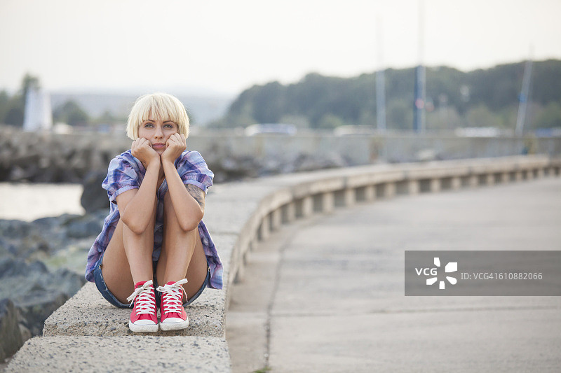 金发女人坐在矮墙上，双手抱头图片素材